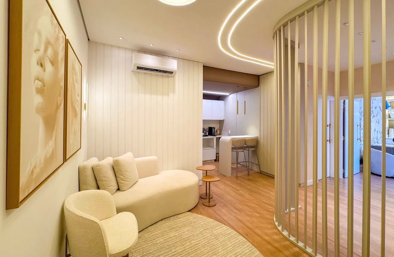 Lounge da recepção com sofá curvo, poltrona em bouclé, quadros em tons de areia e ripado curvo iluminado